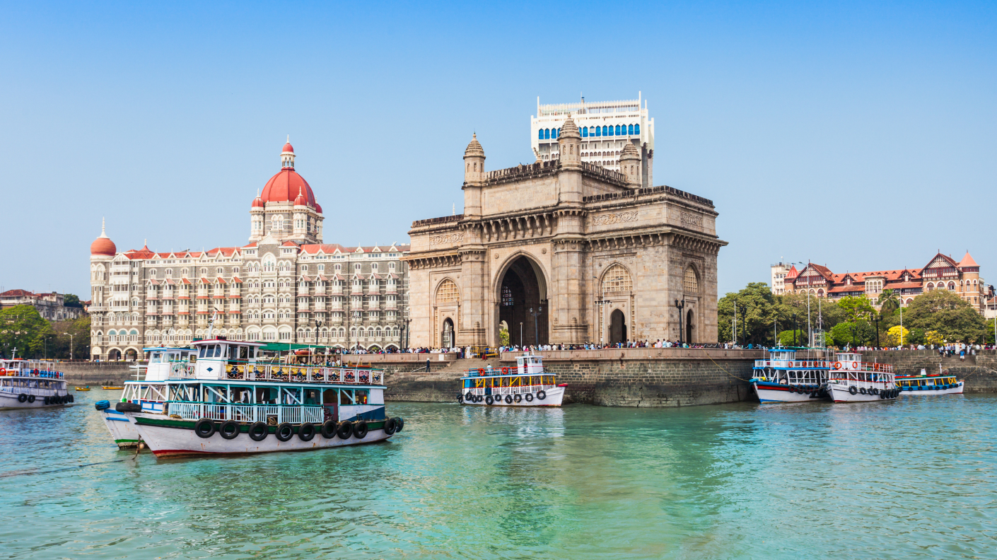 A picture of Bombay Castle in Mumbai with turquoise water in the foreground and a blue cloudless sky overhead.